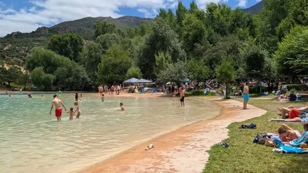 Qué hacer en Málaga con niños este verano 21 Entrada rústica a La Playita en Zahara de la Sierra, rodeada de naturaleza y familias disfrutando del verano.
