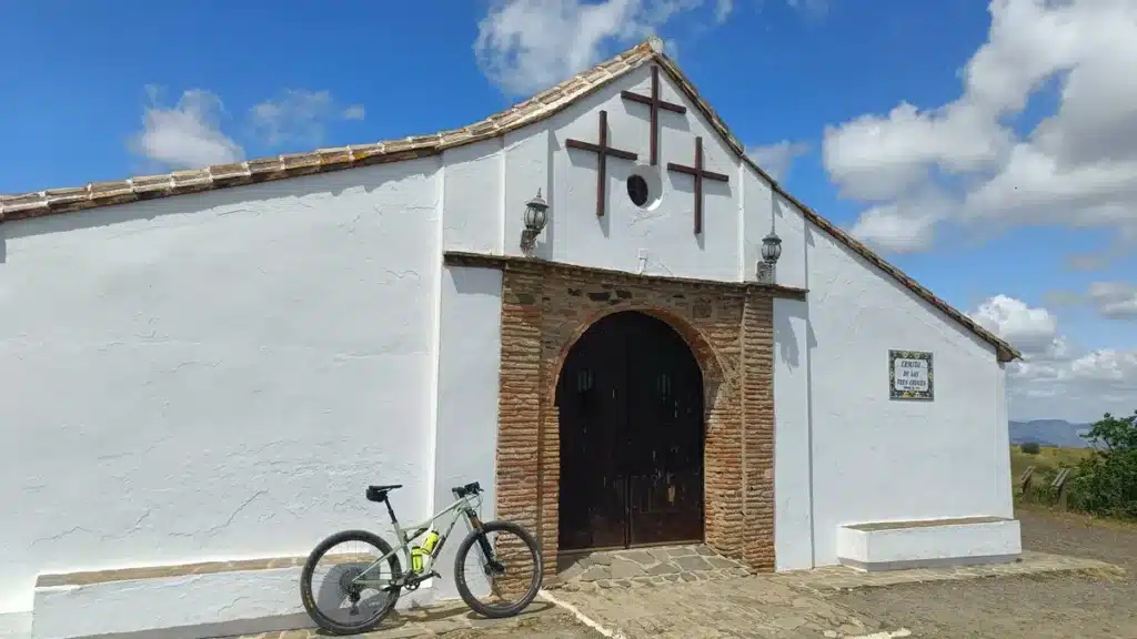 Qué ver en Cártama: historia, naturaleza y gastronomía en el corazón del Valle del Guadalhorce 17 Bicicleta aparcada frente a la Ermita de las Tres Cruces, una capilla blanca bajo un cielo azul brillante en Cártama