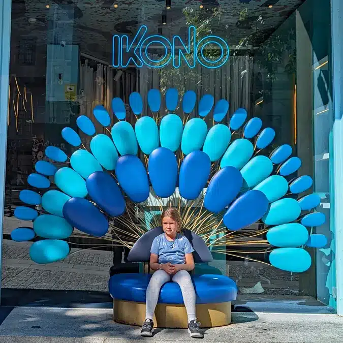 IKONO Madrid: una aventura inmersiva para despertar tu creatividad en familia 1 Entrada de Ikono Madrid con niños, decorada con un trono en forma de pavo real azul.