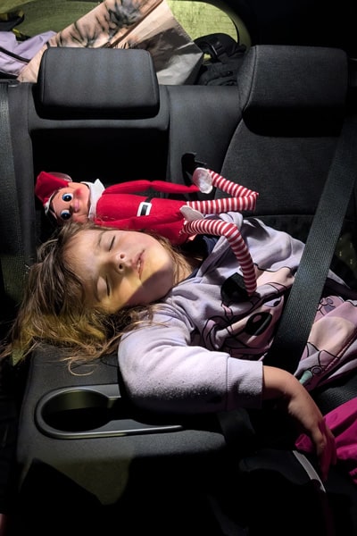 Niña dormida en el coche de alquiler con su elfo de santa village laponia