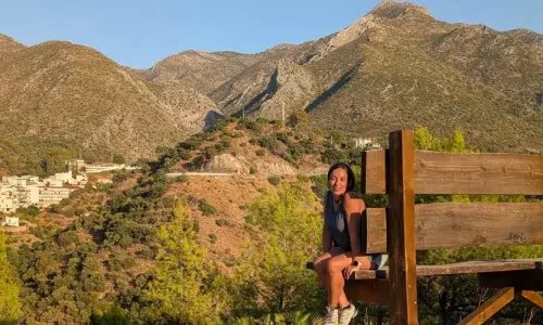 Lucía en el banco gigante de Istán con las montañas de la Sierra de las Nieves al fondo, un mirador icónico del pueblo blanco.