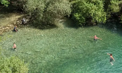 Personas bañándose en pozas de agua cristalina rodeadas de vegetación en el pozo de la cueva del gato.