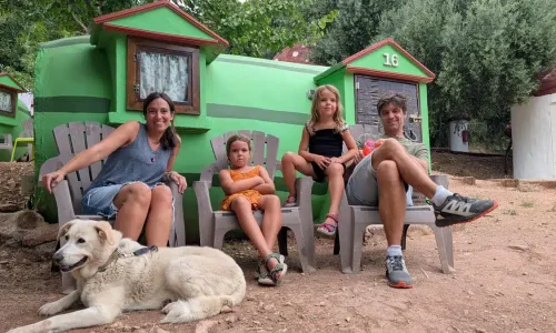 Familia con perro posando frente a una casa en forma de sandía en Villa Sandía, rodeados de naturaleza.